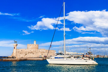 Greece travel, Dodecanese. Rhodes island.  Mandraki Harbor with symbol statue of deer , saillboats and old lighhouse - obrazy, fototapety, plakaty