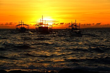 Ship on the tropical sea with waves, under the vivid orange sunset. Evening sun and waves on the...