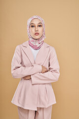 Fototapeta premium Portrait of a beautiful Muslim female model wearing stylish pink office attire with hijab isolated over beige studio background. Fashion, beauty, style concept.