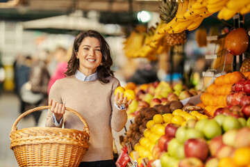 A woman with basket is showing lemons at farmers market and smiling at the camera.