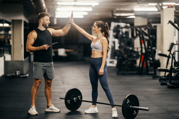A strong sportswoman si giving high five to instructor in a gym.