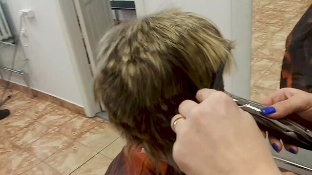 A woman shaves her head bald. A hairdresser shaves a woman's hair with a hair clipper