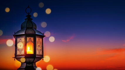 Fototapeta na wymiar Decorative Arabic lantern with a glowing burning candle, in the evening against the background of the evening sky at sunset, copy space. Muslim Holy Month Ramadan Kareem background