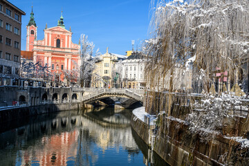 Fototapeta na wymiar Lubiana 02 - vista della città col fiume e neve. Palazzi e un ponte riflessi nell'acqua.