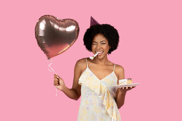 Playful African American woman with curly hair winking and biting a party horn