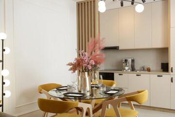 Dining table in the kitchen with yellow wooden chairs and pink flowers bouquet in the vase