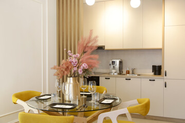 Dining table in the kitchen with yellow wooden chairs and pink flowers bouquet in the vase