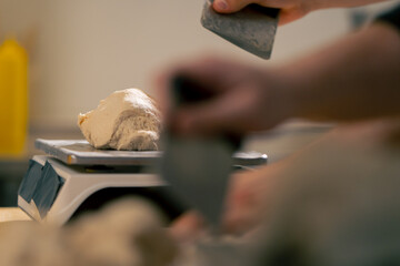 Close-up of a baker cutting off excess dough on scale in a professional kitchen - obrazy, fototapety, plakaty