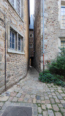 Fototapeta na wymiar Vertical photo of the picturesque very narrow alley of the old town of Le Mans in France, old style inner courtyard, stone houses