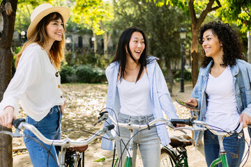 Young group of women with rental bikes hanging out at city street, enjoying summer vacation in...