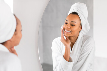 Black millennial woman applying micellar water with cotton pad indoors