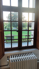 Detail of a nice window in an old luxury rustic mansion. Through the window you can see the large green garden. Under the window is the large iron heater that runs on hot water.