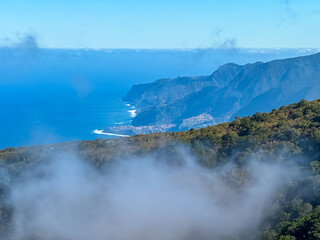 Naklejka na ściany i meble Panoramic view of majestic coastline of Atlantic Ocean seen from mountain top of Fanal, Madeira island, Portugal, Europe. Clouds coming up from sea. Tranquil serene atmosphere on sunny summer day