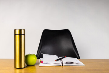 Office supplies and drinkware on a wood desk book, apple, thermos, pen