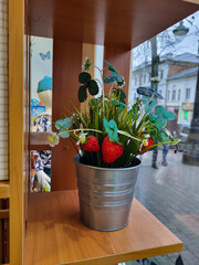 There is a small decorative iron bucket with a strawberry bush on the window display.