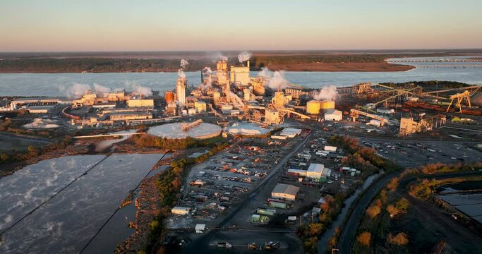 Sunrise view of a paper mill in Brunswick, Georgia, with visible effluent ponds and industrial activity, suggesting environmental concerns like air and water pollution.