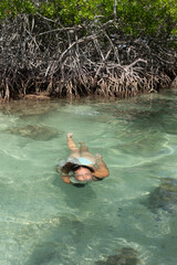 Girl swimming under turquoise sea water with a mangrove swamp behind her