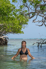 Woman in the shadows of a mangrove swamp in the clear turquoise water with the sea in the background