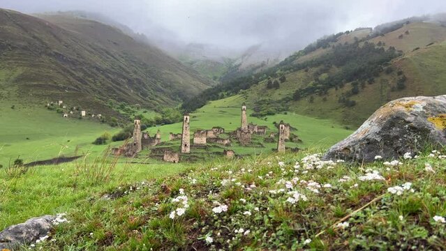 View of the medieval Targim tower complex in the Caucasus mountains surrounded by greenery. The Caucasus Mountains on a cloudy day in Ingushetia. Russia, 4K.
