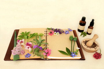 Preparing aromatherapy essential oil with flowers, herbs, wildflowers used in natural herbal medicine remedies with tincture bottles, recipe notebook on hemp paper 
