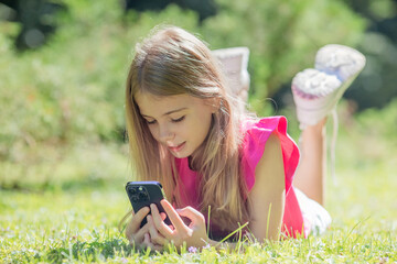 beautiful teenage girl lies on green grass with a smartphone in her hands in the park, close up.