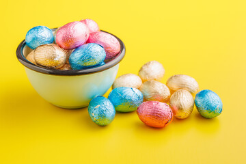 Easter chocolate eggs wrapped in aluminium foil on yellow background.