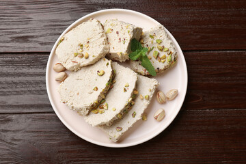 Pieces of tasty halva with pistachios and mint on wooden table, top view