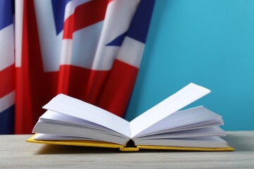 Learning foreign language. Open book on wooden table near flag of United Kingdom, space for text