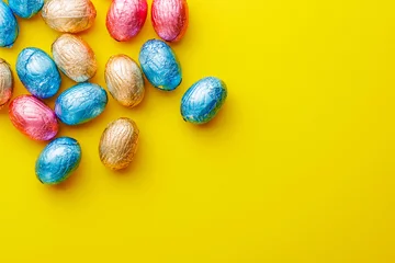 Fotobehang Easter chocolate eggs wrapped in aluminium foil on yellow background. Top view. © Jiri Hera
