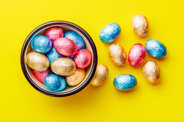 Easter chocolate eggs wrapped in aluminium foil in bowl on yellow background. Top view.