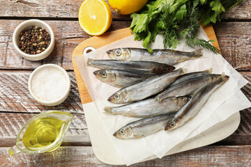 Fresh raw sprats and products on wooden table, flat lay