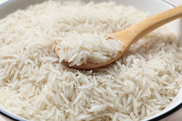 Raw basmati rice with wooden spoon in bowl, closeup