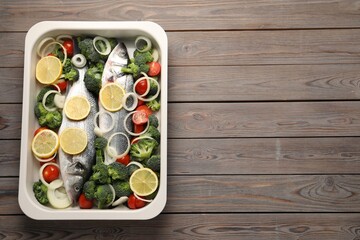 Fototapeta na wymiar Raw fish with vegetables and lemon in baking dish on wooden table, top view. Space for text