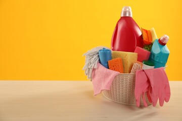 Different cleaning products in basket on wooden table against yellow background, space for text