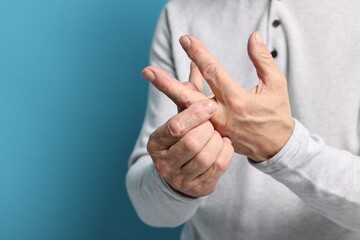 Arthritis symptoms. Man suffering from pain in hand on light blue background, closeup. Space for text