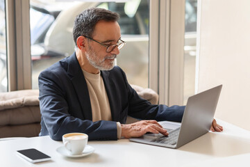 Concentrated mature businessman with glasses typing on a laptop in a café