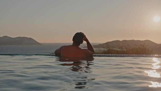 A handsome mixed race man in a view pool, looking at the sunset