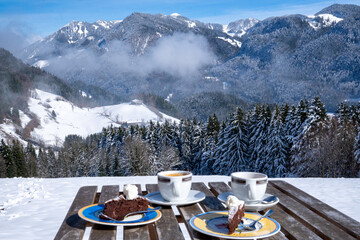 View over a set table with coffee and cake to the Chiemgau Alps and Geigelstein (1808 m), Bavaria, Germany in winter. - obrazy, fototapety, plakaty