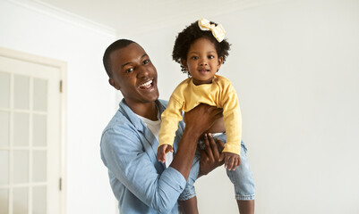 Happy young black father lifting up his pretty little daughter