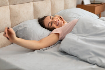 Joyful woman stretching in bed after waking up