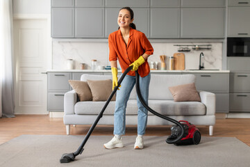 Smiling woman using red vacuum cleaner in modern kitchen