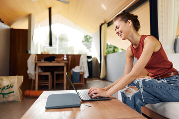 Smiling woman sitting on a comfy sofa with her laptop in a cozy living room She appears to be a...