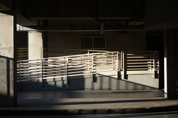 A public garage with heavy concrete architecture. Hard light streams into a passenger pick up and...
