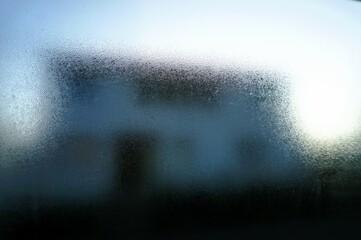 Abstraktes Motiv mit Eisbedeckter Glasscheibe vor weißem Wohnhaus und Himmel bei Frost und Kälte am Morgen im Winter