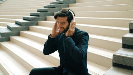 Project manager listening and enjoy music from headphone while sitting at stairs. Professional...