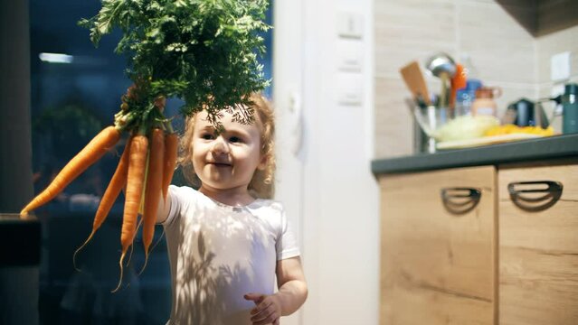 Happy little girl wearing ballerina costume dances with fresh carrots in the kitchen. Healthy eating concept