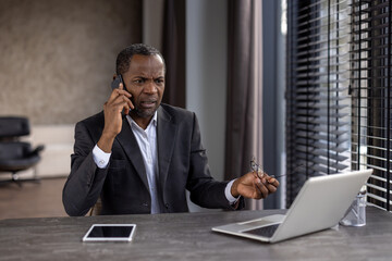 Senior businessman in suit engaged in a serious phone conversation at his office desk