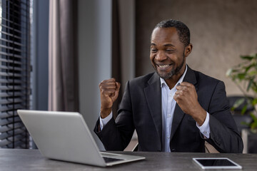 Joyful african american businessman celebrating success at office desk