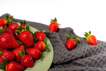 Red strawberries on a gray towel and a light green plate on a white background.