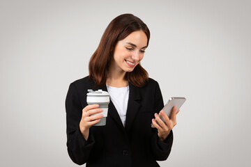 Multitasking businesswoman in a stylish black suit browsing her smartphone with a smile